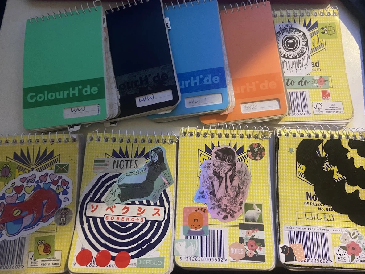 a picture of 7 notebooks laid out, each with different coloured covers and stickers